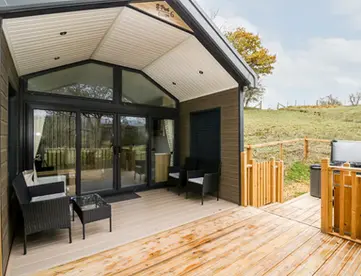 Modern cabin with large deck, outdoor seating, hot tub, and hilly landscape.