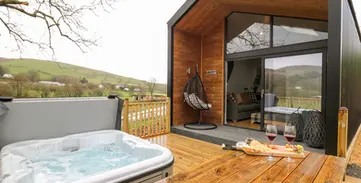 Contemporary cabin, bubbling hot tub, wine, and scenic hilly landscape.