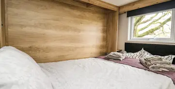 Modern bedroom with comfortable white bedding, wooden feature wall, and window view.