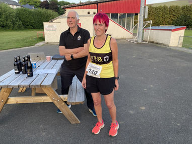 Woman in race bib stands near man and table with bottles, EV5K RACE.