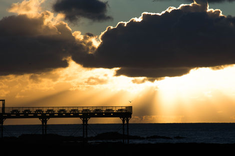 Pier sunset silhouette, sun rays through clouds