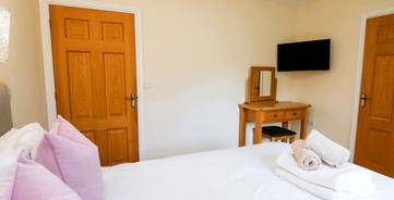 Inviting bedroom with white bed, pink pillows, wooden doors, dressing table, TV.