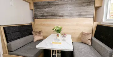Cozy dining nook with gray cushioned benches, small table, and wood paneling.