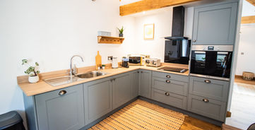 Modern kitchen with sleek grey cabinets, wooden beams, light counter, woven rug.