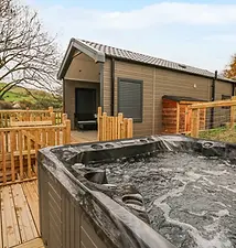 Bubbling hot tub on wooden deck outside a modern cabin.