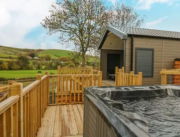 Hot tub on wooden deck outside a modern cabin with scenic hills.