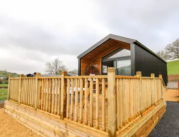 Modern black cabin with large wooden deck overlooking green hills.