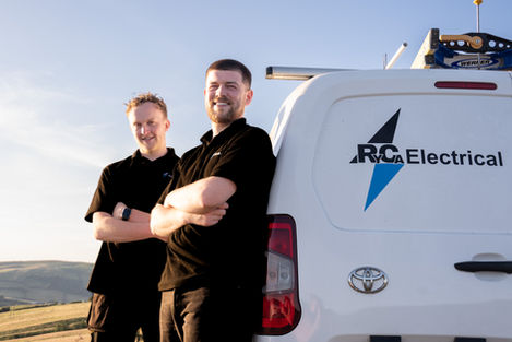 Ryca Electricals team portrait: two smiling electricians stand by their van