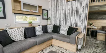 Modern living room with grey L-shaped sofa, patterned rug, wooden details.