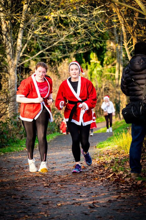 Two women in Santa suits jog