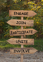 Wooden signpost with ENGAGE, JOIN, PARTICIPATE, UNITE, INVOLVE for community involvement.
