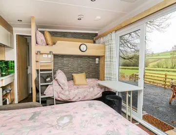 Compact bedroom with bunk beds, sofa, and sliding door overlooking green hills.