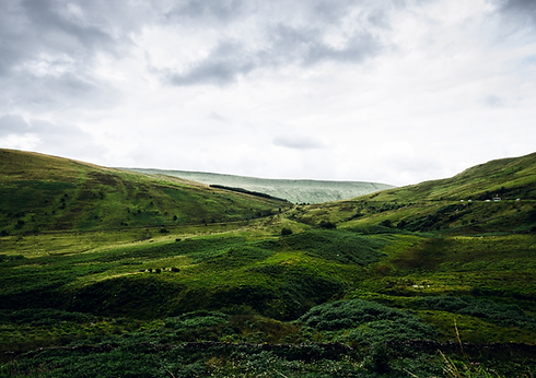Green rolling hills and valley under a dramatic cloudy sky.