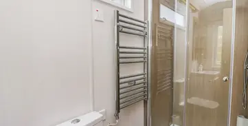 Bright modern bathroom with toilet, chrome heated towel rail, glass shower.