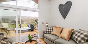 Modern living room, grey sofa, hot tub on deck, countryside views.