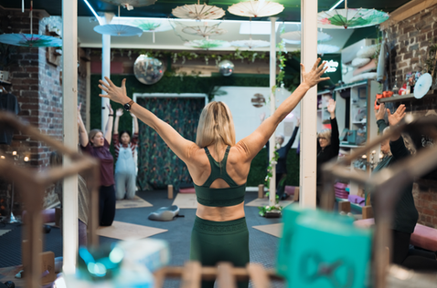 Serena leading Serenity Yoga class with arms raised, several students stretching, inside