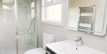 Modern bathroom with glass shower, toilet, sink, mirror, towel rail.