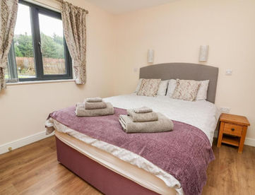 Comfortable bedroom with double bed, purple throw, folded towels, window.
