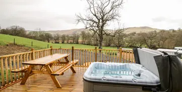 Wooden deck with hot tub, picnic table, and scenic green hills background.