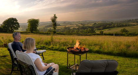 Woman relaxing by fire pit, scenic sunset view