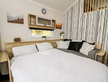 Cozy bedroom with wooden bed, white duvet, black and white pillows, small window.