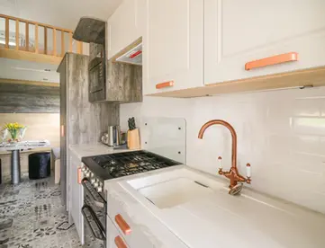 Modern compact kitchen with white cabinets, copper faucet, and gas stove.