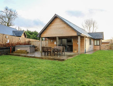 Wooden lodge with patio, outdoor seating, hot tub, and green lawn.