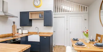 Modern kitchen dining area, dark blue cabinets, wood counters, yellow clock.