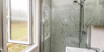 Modern bathroom with glass shower, white sink, and open window.