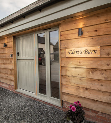 Modern barn conversion entrance with "Eleri's Barn" sign and wood cladding.