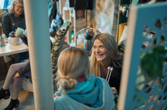 Serena smiling, talking with a friend, surrounded by plants and decor.