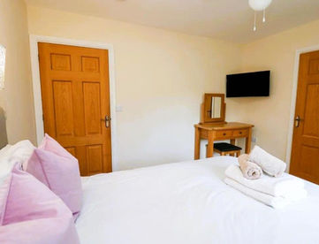 Bright bedroom with white bed, pink pillows, wooden doors, TV, dressing table.