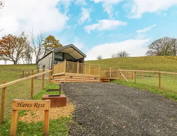 Modern cabin with 'Hares Rest' sign on a grassy hillside.