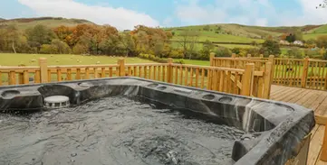 Outdoor hot tub on deck overlooking scenic green hills.