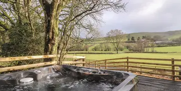 Outdoor bubbling hot tub next to fence overlooking green valley.