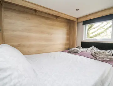 Bedroom with white bed, wooden paneling, and window overlooking trees.