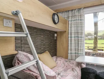 Bunk bed with patterned bedding by a window overlooking green fields.
