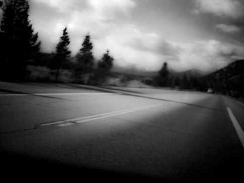 Blurry image of a road lined by trees, with a car in the distance