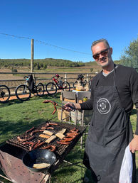Man grilling sausages outdoors, bikes in background
