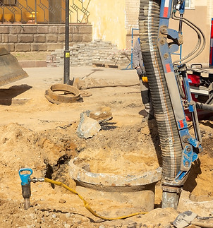 Workers use a suction excavator based on a truck to sample soil in a well for communicatio