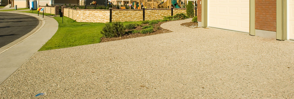 Gravel driveway leading to a garage, bordered by manicured shrubs and grass