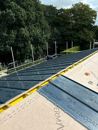 A worker installs dark metal roof panels on a sloped structure