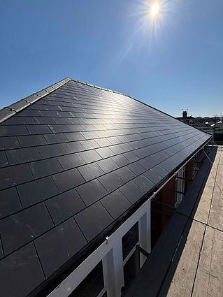 A sunlit roof with sleek dark slate tiles under a clear blue sky, capturing a bright