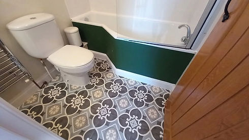 Small bathroom showing a white toilet, bathtub with glass shower screen, and black-and-white patterned floor tiles