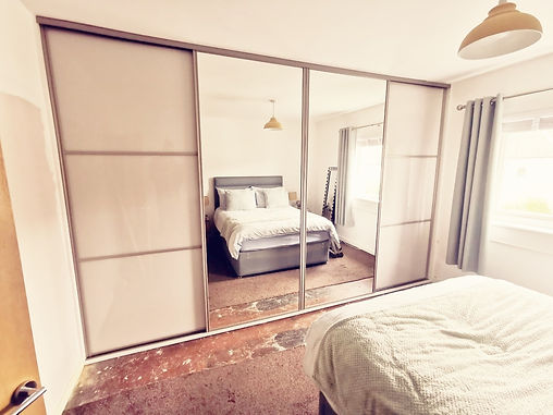 A cozy, minimalist bedroom featuring a neatly made double bed with grey and white bedding