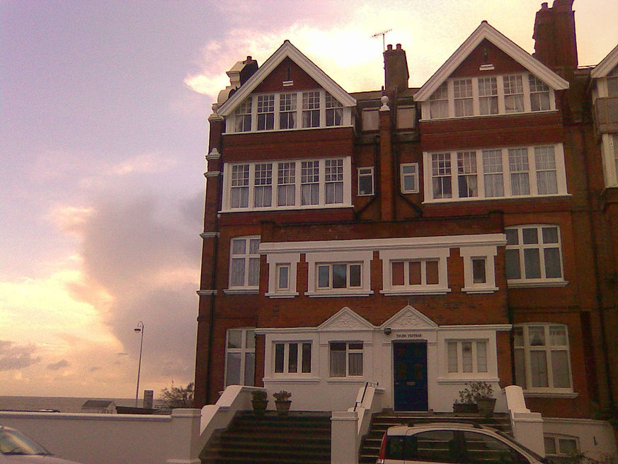 Large brick building with numerous white-framed windows under a cloudy sky near sunset