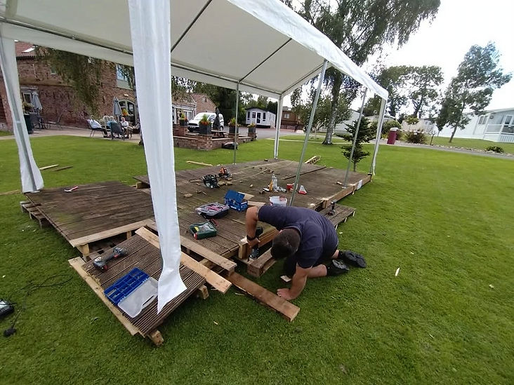 Handyperson working on constructing an outdoor wooden deck frame in a lawn garden