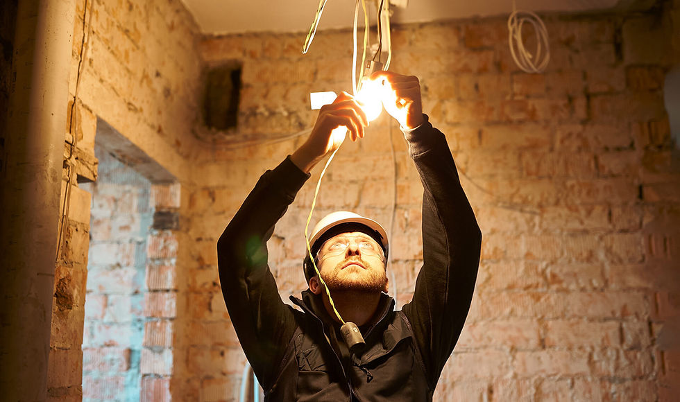 Electrician in a hard hat installs wiring under bright light in a brick-walled room