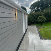 A modern grey building with sleek wall lights stands beside a shiny wet patio