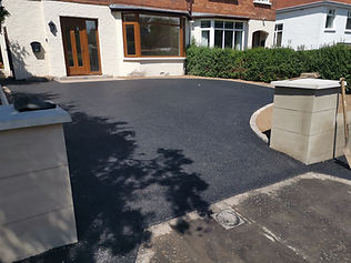 Driveway leads to white house with bay windows and shrubs